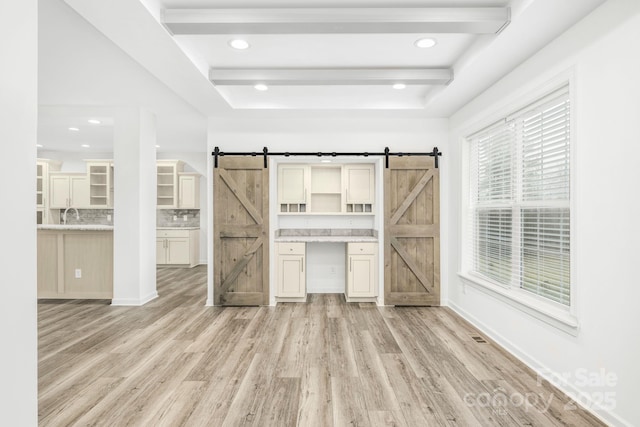 unfurnished living room featuring a barn door, light hardwood / wood-style flooring, beamed ceiling, and sink