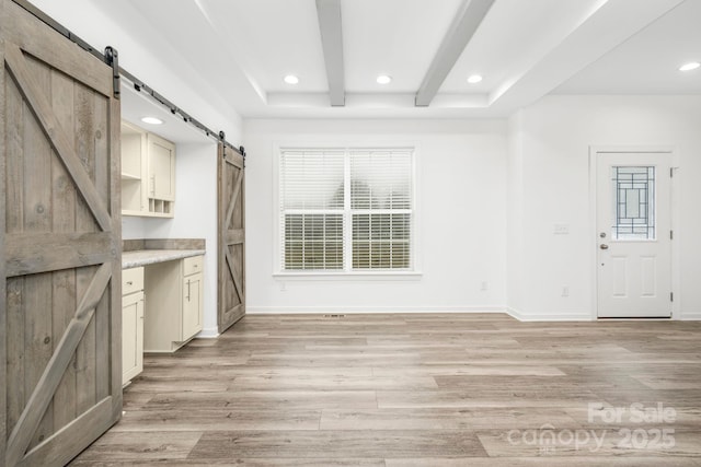 interior space featuring beamed ceiling, a barn door, and light hardwood / wood-style flooring