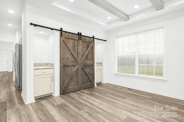 interior space with a barn door, light hardwood / wood-style flooring, and beamed ceiling