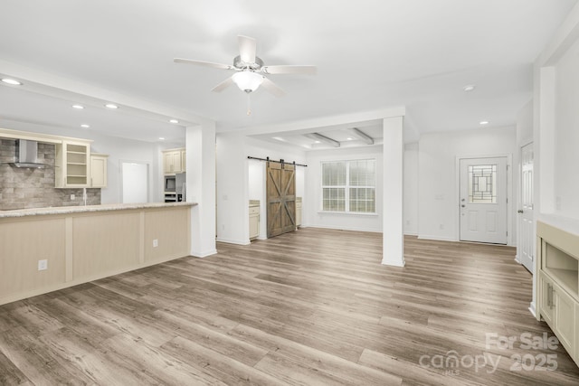 unfurnished living room featuring a barn door, ceiling fan, beamed ceiling, and light wood-type flooring