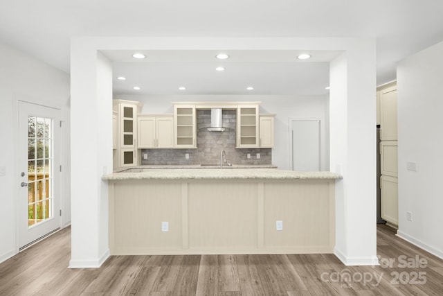 kitchen featuring sink, wall chimney exhaust hood, decorative backsplash, light stone countertops, and light wood-type flooring