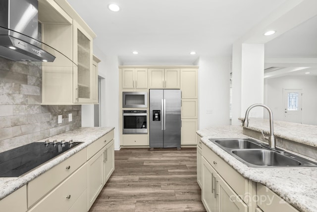 kitchen with sink, wall chimney exhaust hood, cream cabinetry, decorative backsplash, and appliances with stainless steel finishes