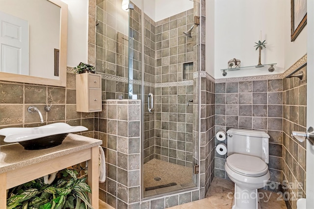 bathroom with toilet, tile walls, a shower with shower door, and sink