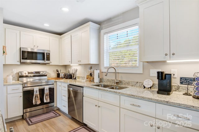 kitchen with light stone countertops, stainless steel appliances, sink, light hardwood / wood-style flooring, and white cabinets