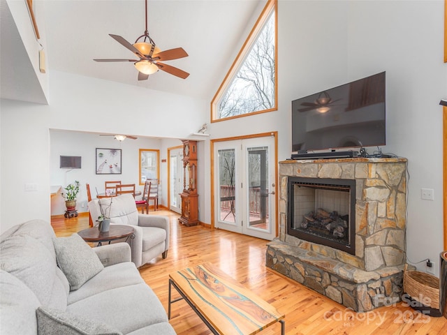 living room with high vaulted ceiling, a stone fireplace, ceiling fan, and light hardwood / wood-style floors