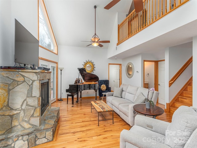 living room with ceiling fan, a fireplace, high vaulted ceiling, and light wood-type flooring