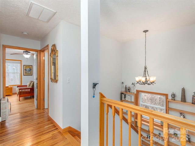 hall with a notable chandelier, light hardwood / wood-style floors, and a textured ceiling