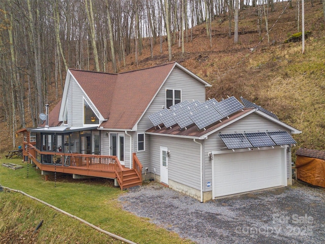 rear view of house with a lawn, solar panels, a garage, and a deck