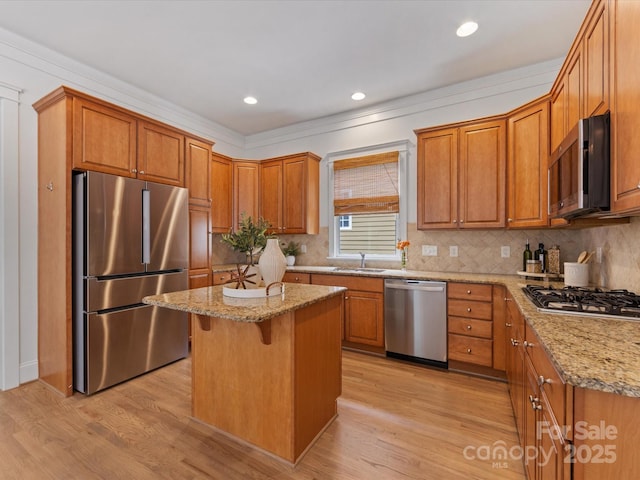 kitchen featuring sink, stainless steel appliances, light stone counters, a breakfast bar, and a kitchen island