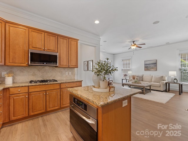 kitchen with a center island, tasteful backsplash, light stone counters, plenty of natural light, and appliances with stainless steel finishes