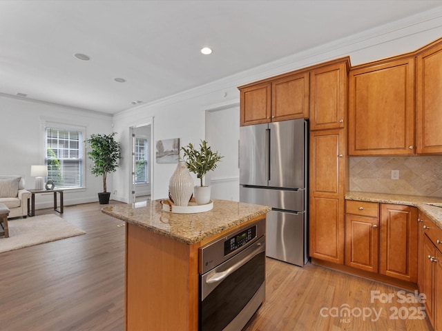 kitchen featuring crown molding, decorative backsplash, light stone countertops, appliances with stainless steel finishes, and a kitchen island