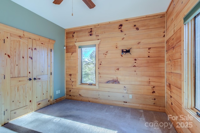 unfurnished bedroom featuring carpet, ceiling fan, and wood walls