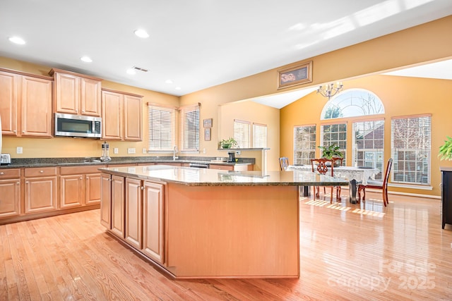 kitchen with appliances with stainless steel finishes, dark stone countertops, a chandelier, light hardwood / wood-style floors, and a kitchen island