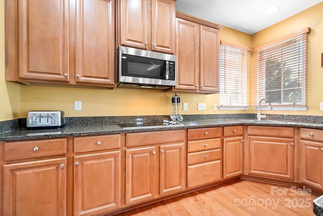 kitchen with dark stone counters, stovetop, light hardwood / wood-style floors, and sink