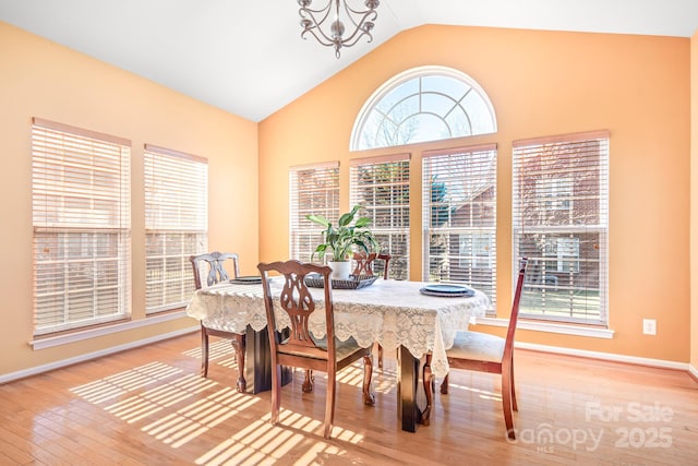 dining space with a wealth of natural light, a chandelier, vaulted ceiling, and hardwood / wood-style flooring