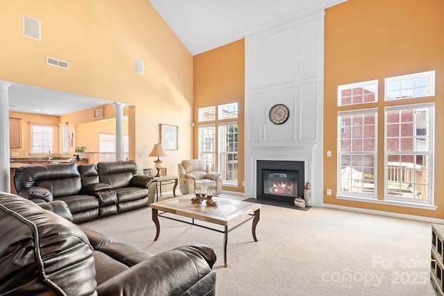 living room featuring light colored carpet, a fireplace, high vaulted ceiling, and decorative columns