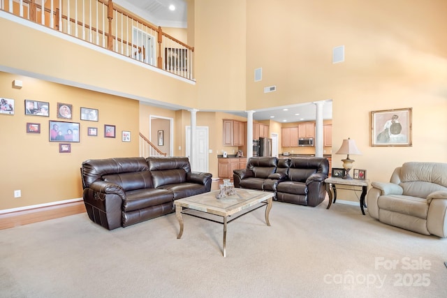 living room with decorative columns, a towering ceiling, and light colored carpet