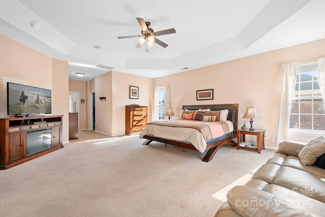 carpeted bedroom featuring ceiling fan, multiple windows, and a tray ceiling