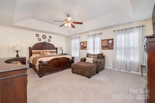 bedroom with light colored carpet, a raised ceiling, and ceiling fan