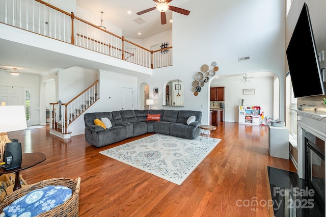 living room with hardwood / wood-style flooring, ceiling fan, and a towering ceiling