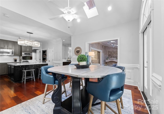 dining room with dark hardwood / wood-style flooring, a skylight, ceiling fan, and brick wall