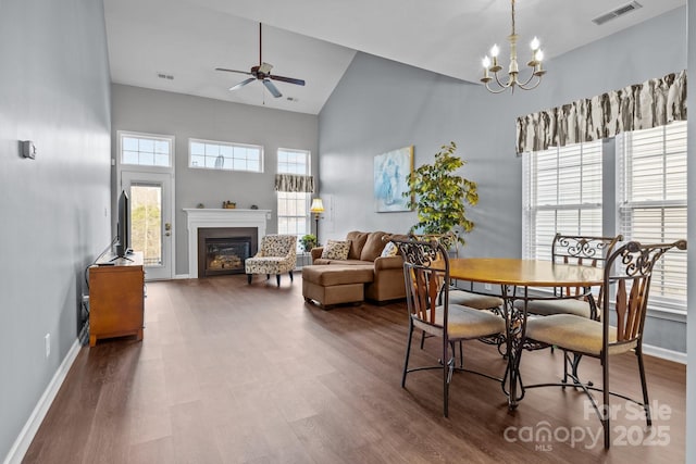 dining area featuring plenty of natural light, dark hardwood / wood-style flooring, ceiling fan with notable chandelier, and a high ceiling