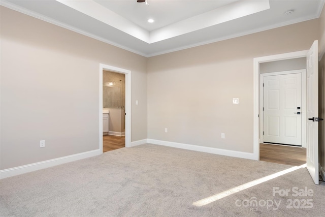 unfurnished bedroom with a tray ceiling, ensuite bath, crown molding, and light colored carpet