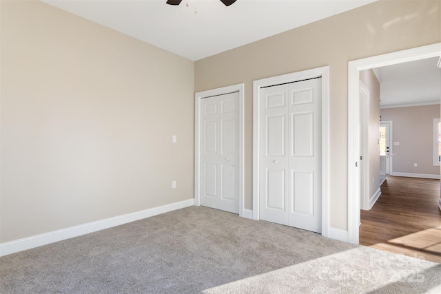 unfurnished bedroom with carpet flooring, two closets, ceiling fan, and crown molding