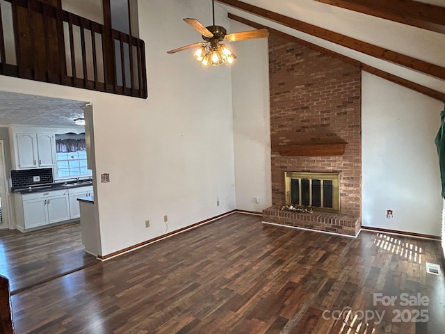 unfurnished living room with dark wood-type flooring, high vaulted ceiling, a brick fireplace, ceiling fan, and beam ceiling