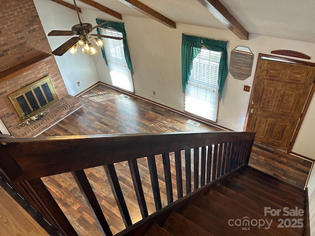 stairway featuring ceiling fan, vaulted ceiling with beams, wood-type flooring, a textured ceiling, and a fireplace