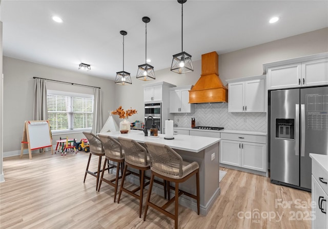 kitchen featuring premium range hood, a center island with sink, a kitchen bar, white cabinetry, and stainless steel appliances