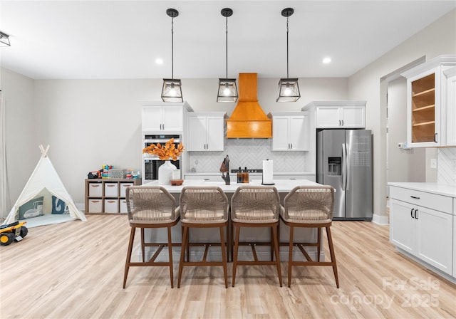 kitchen featuring a breakfast bar, stainless steel appliances, white cabinetry, and premium range hood