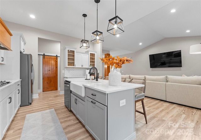 kitchen with a center island with sink, a kitchen breakfast bar, a barn door, white cabinetry, and stainless steel appliances