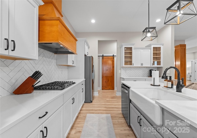 kitchen featuring pendant lighting, sink, a barn door, white cabinetry, and stainless steel appliances