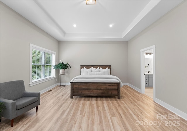 bedroom featuring ensuite bathroom, a raised ceiling, and light hardwood / wood-style floors