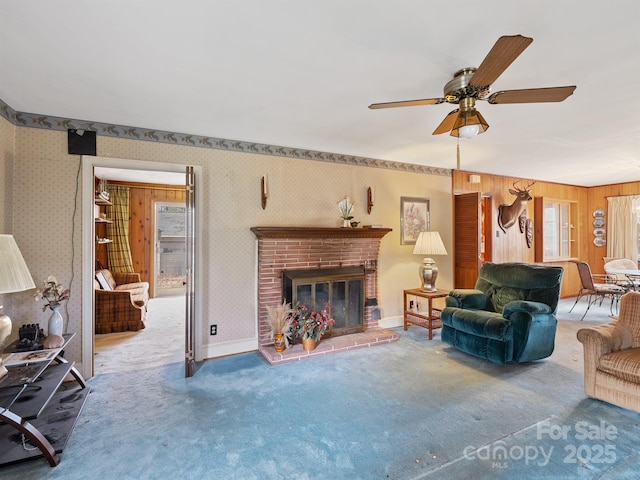 living room with carpet flooring, a brick fireplace, ceiling fan, and wooden walls