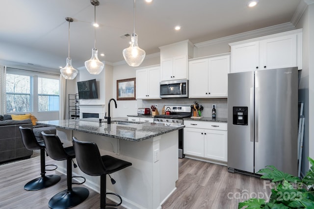 kitchen featuring stainless steel appliances, sink, pendant lighting, a center island with sink, and white cabinets