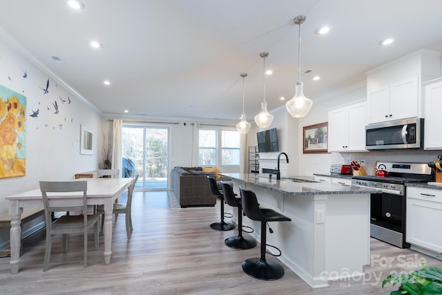 kitchen featuring white cabinets, sink, an island with sink, decorative light fixtures, and stainless steel appliances