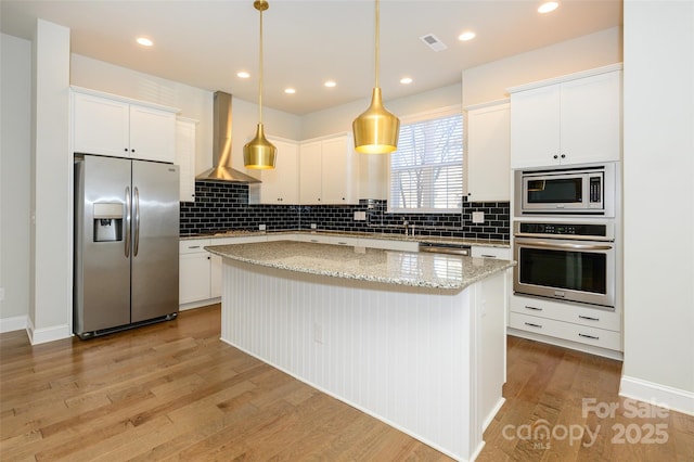 kitchen featuring a center island, visible vents, light wood-style flooring, appliances with stainless steel finishes, and wall chimney exhaust hood