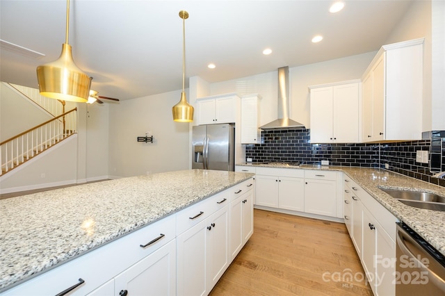 kitchen with light wood finished floors, tasteful backsplash, wall chimney exhaust hood, stainless steel appliances, and white cabinetry