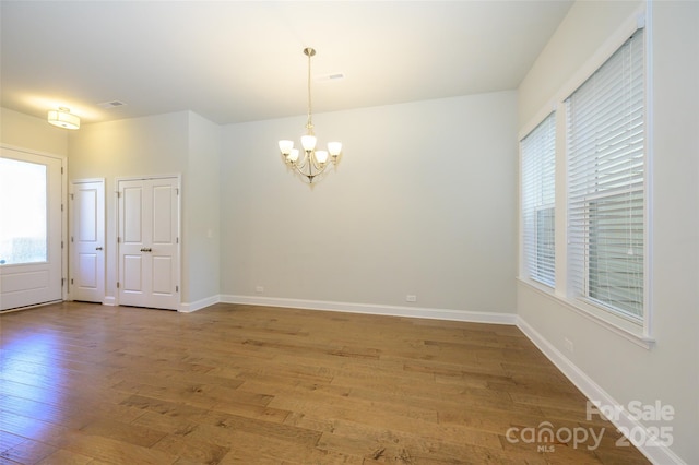 spare room featuring hardwood / wood-style flooring, baseboards, and a notable chandelier