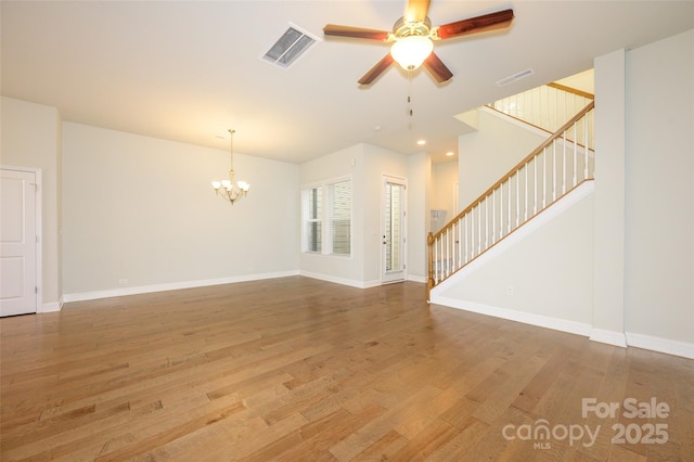 unfurnished living room featuring stairs, ceiling fan with notable chandelier, wood finished floors, and visible vents