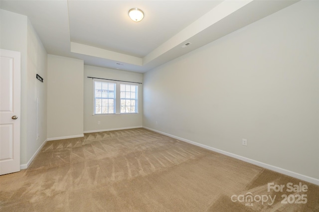 spare room featuring a tray ceiling, light carpet, and baseboards