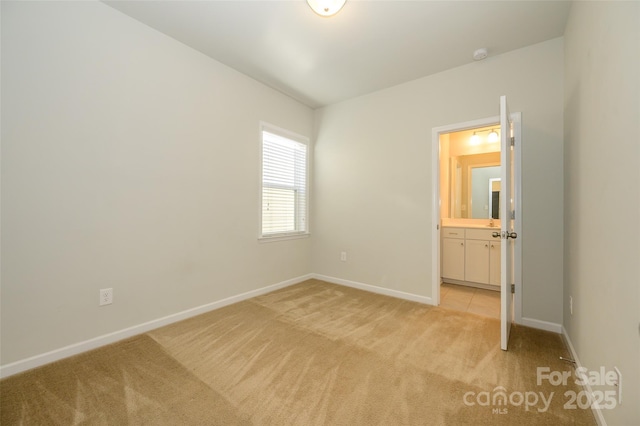 unfurnished bedroom with light colored carpet, ensuite bath, and baseboards