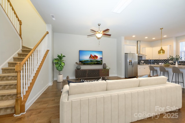 living area with ceiling fan, recessed lighting, wood finished floors, baseboards, and stairway