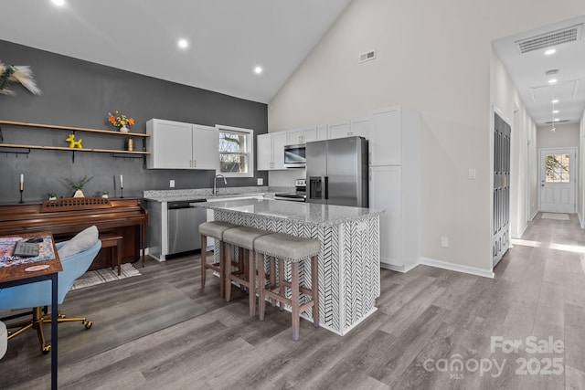 kitchen with white cabinetry, a center island, stainless steel appliances, high vaulted ceiling, and light wood-type flooring