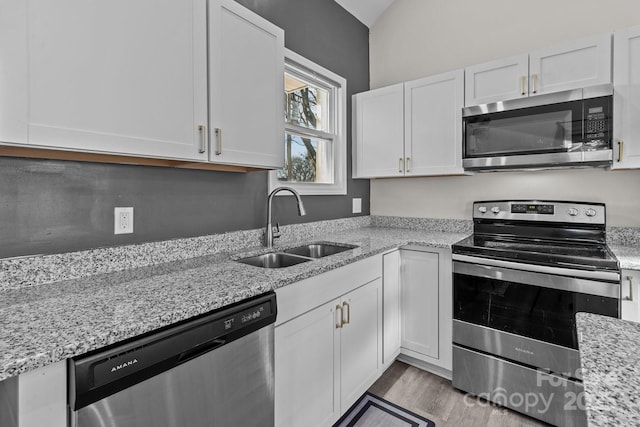 kitchen with white cabinets, sink, vaulted ceiling, light stone countertops, and appliances with stainless steel finishes