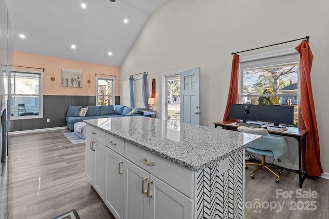 kitchen featuring white cabinetry, light stone counters, light hardwood / wood-style floors, vaulted ceiling, and a kitchen island