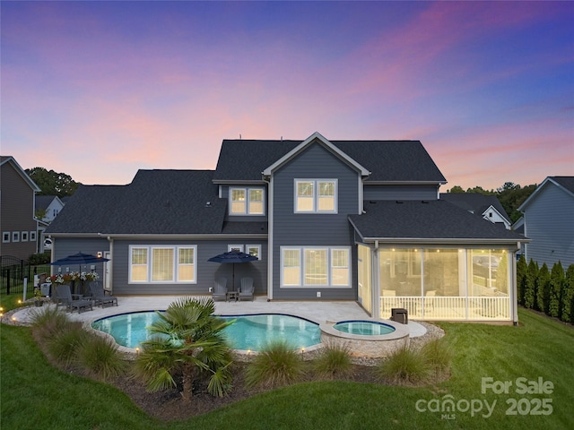 back house at dusk with a lawn, a patio area, and a pool with hot tub