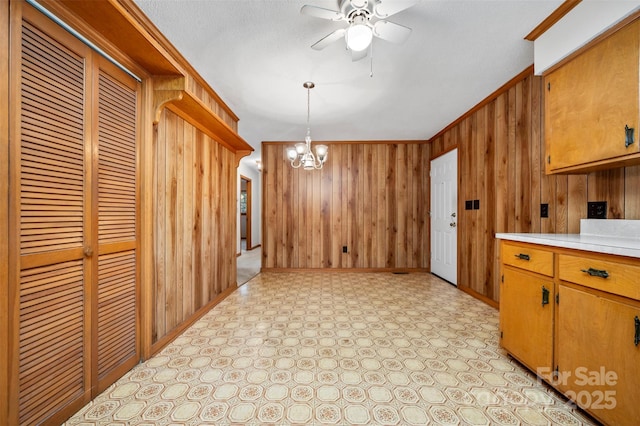 kitchen with ceiling fan with notable chandelier, ornamental molding, hanging light fixtures, and wooden walls